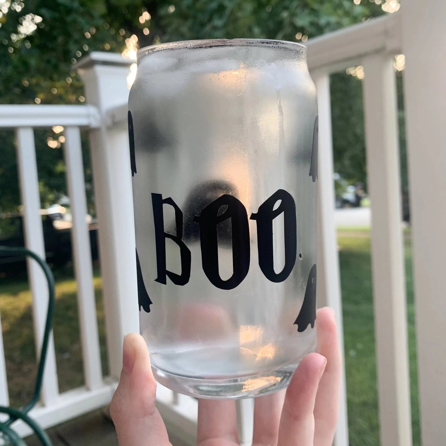 Hand holding boo ghost glass can filled with ice cold water.