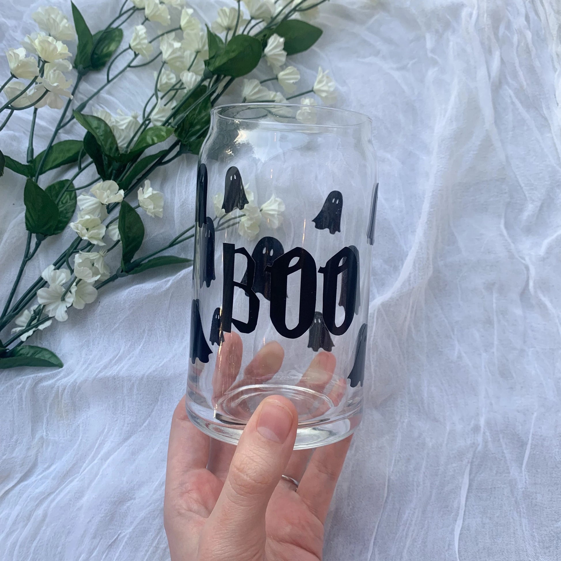 Hand holding a clear cup with black lettering and mini black ghosts all around.