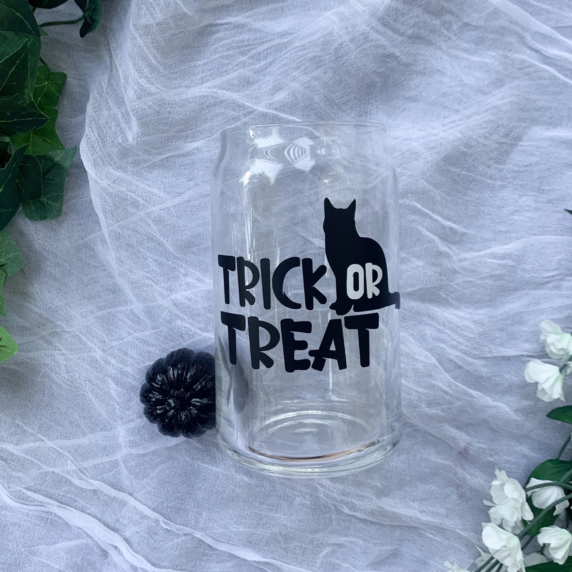 Clear glass cup with black trick or treat lettering with black cat design .