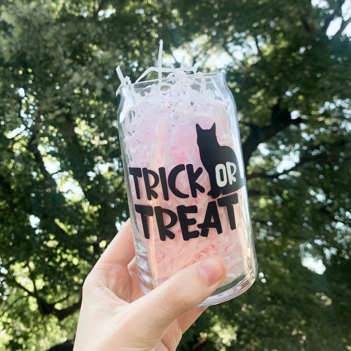 A hand holding trick or treat glass Halloween cup up in the air with a tree as the background.