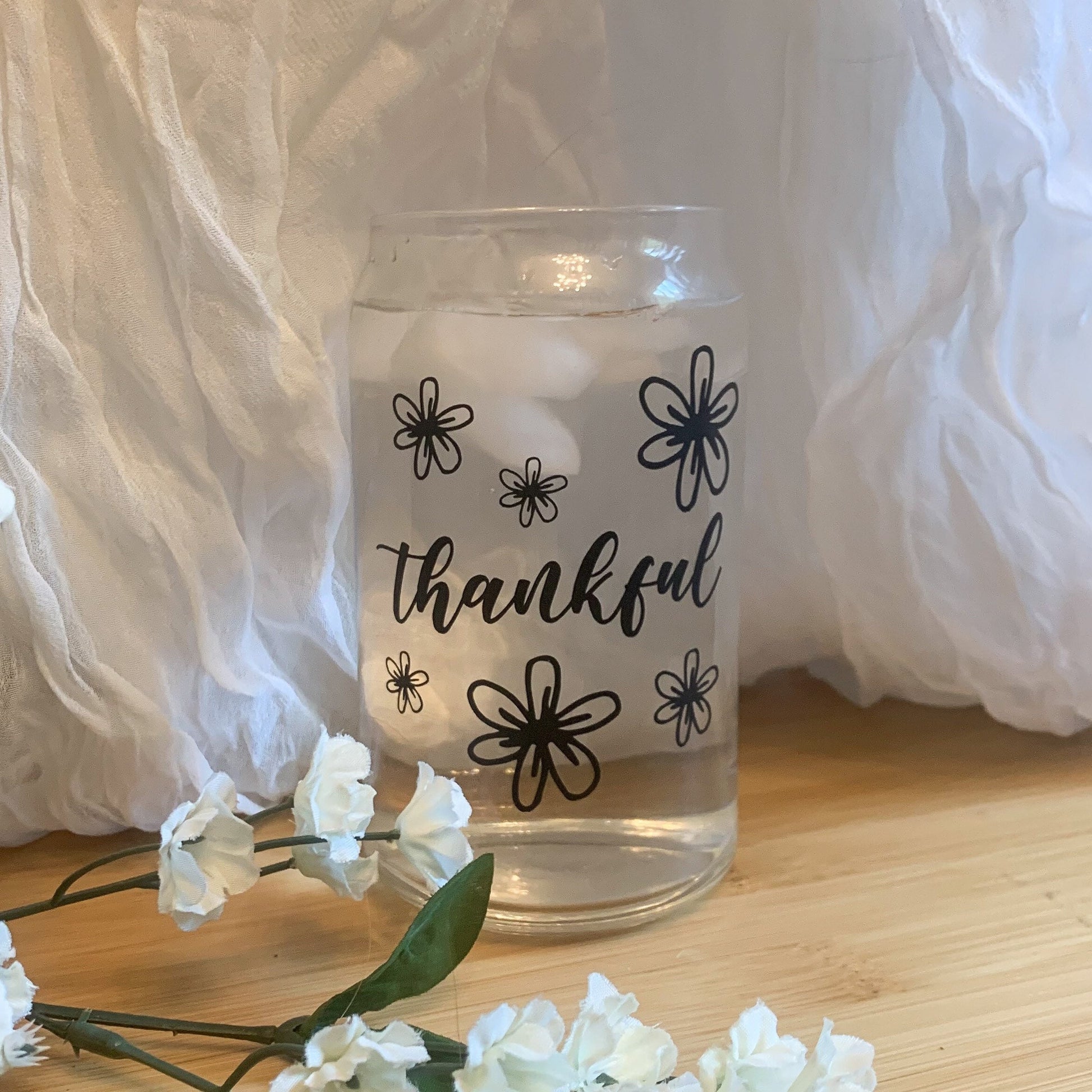 A floral thankful glass cup is filled with ice cold water.