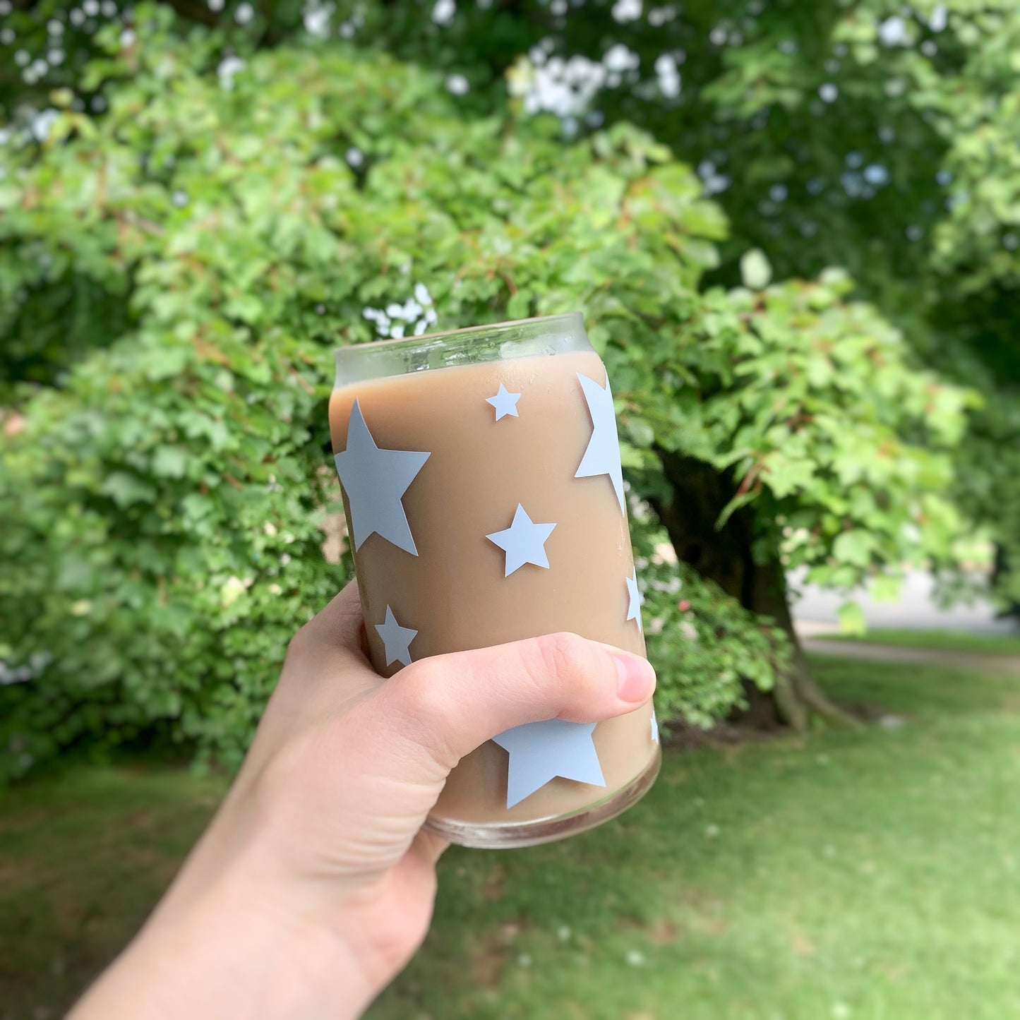 Hand holding star glass filled with iced coffee in front of greenery.