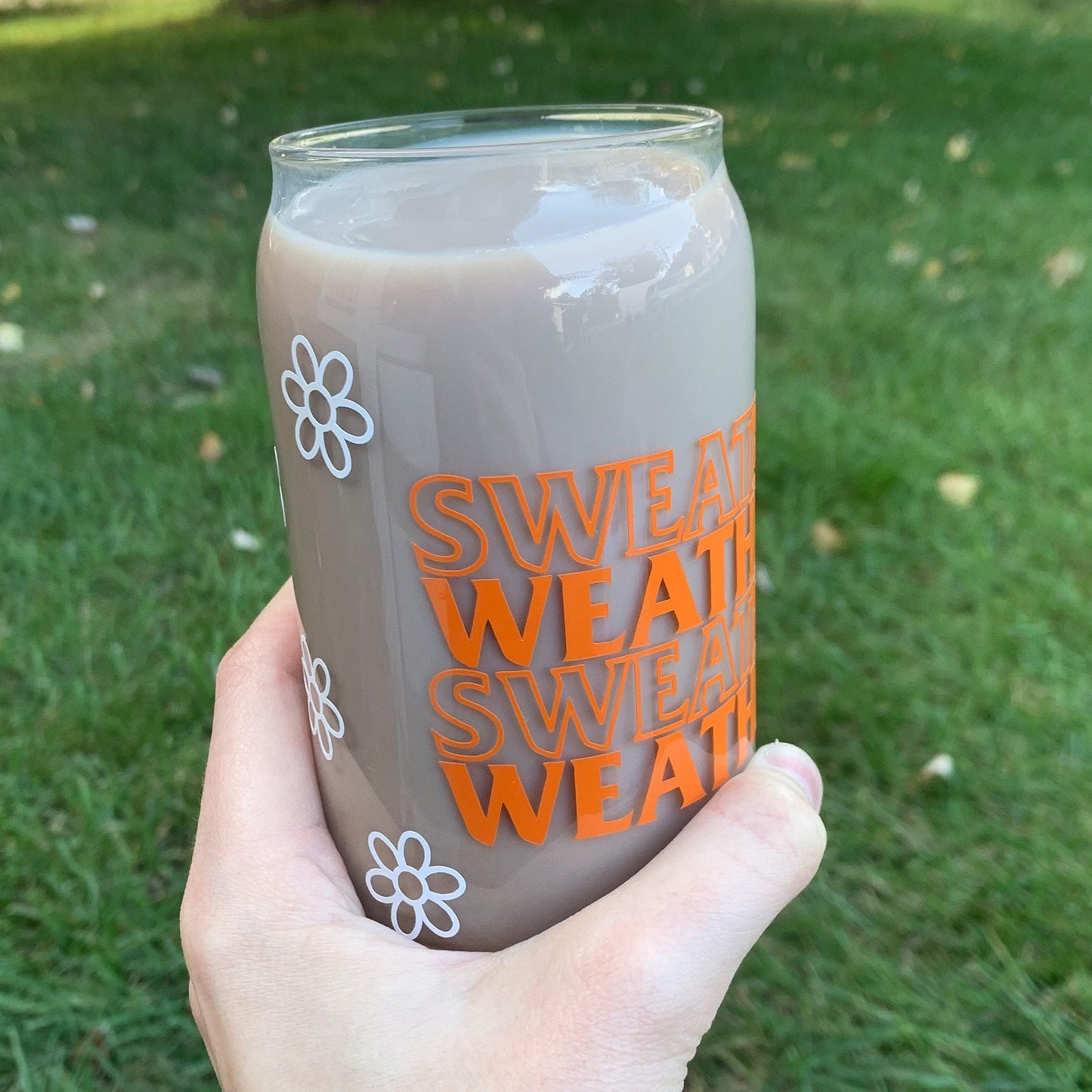 Glass cup with sweater weather written in orange lettering and white flowers surrounding entire cup.