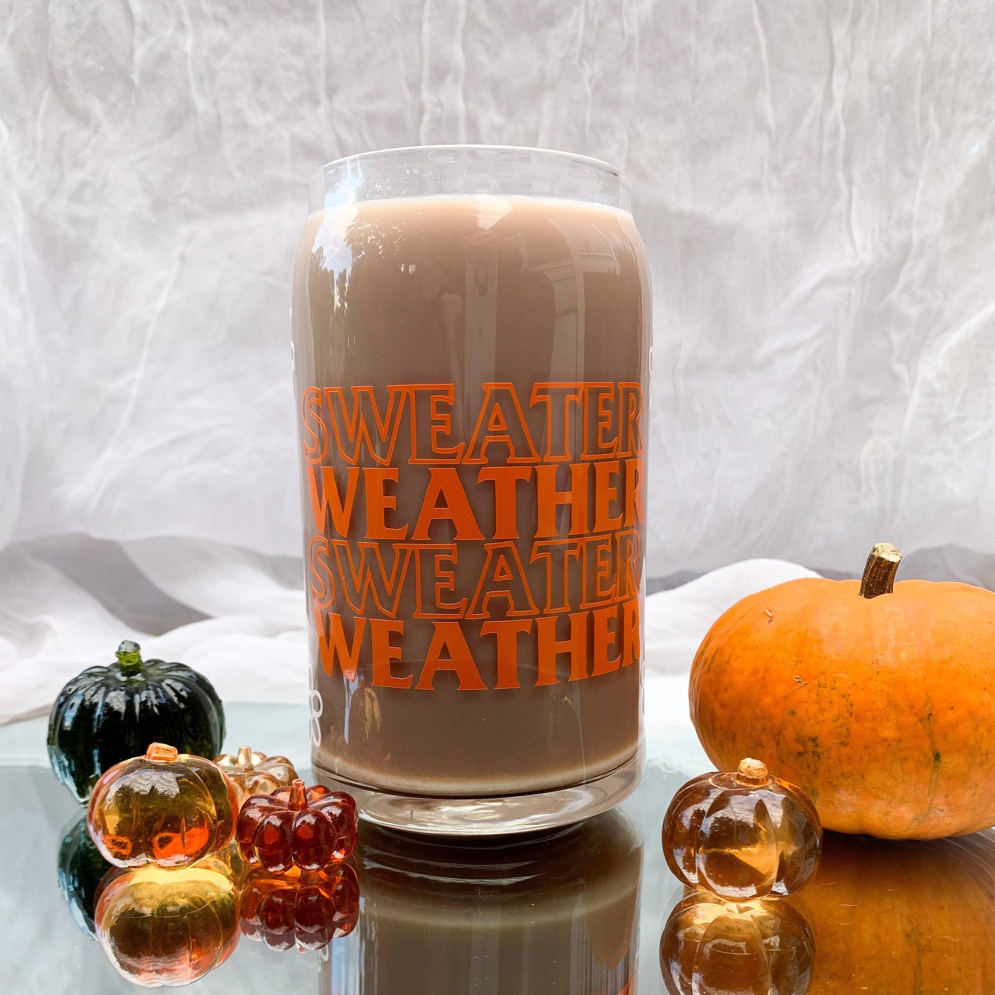 Sweater Weather glass cup filled with coffee and surrounded by real and acrylic mini pumpkins.